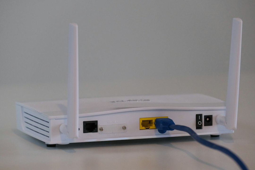 White wireless router with two antennas on a flat surface; blue Ethernet cable plugged into the yellow WAN port.